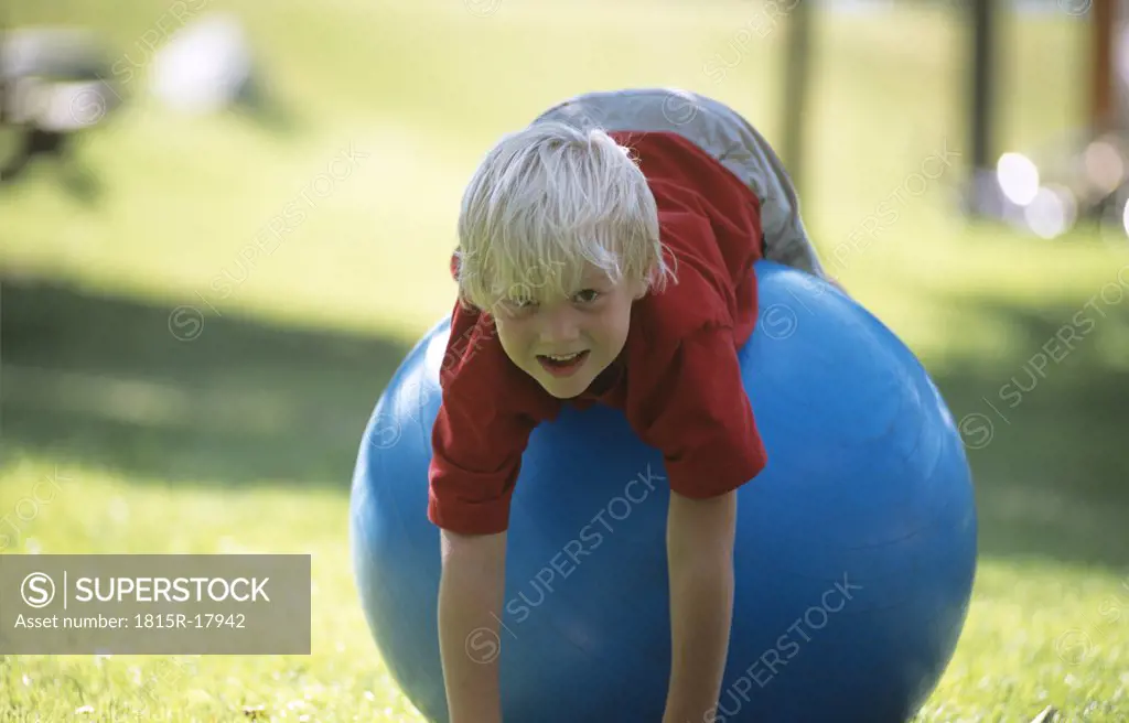Boy (6-7) lying on big blue rubber ball, portrait