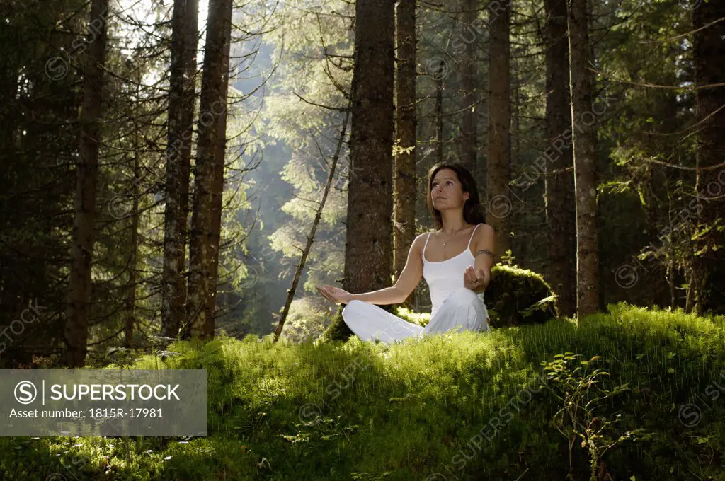 Woman meditating in forest, looking away, low angle view