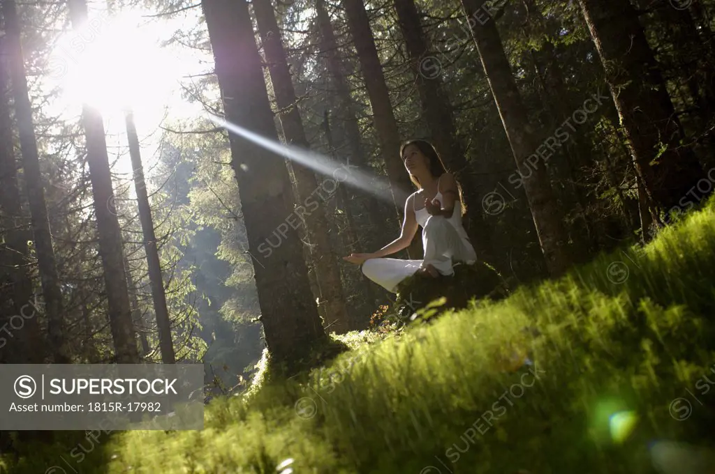 Woman meditating in forest, low angle view