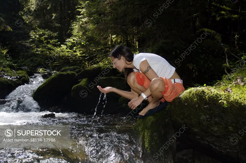 Austria, woman drinking water from stream in forest