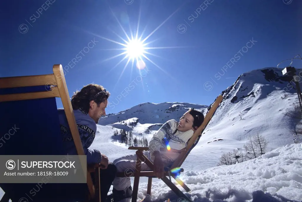 Young couple sitting on deckchairs in alps, smiling