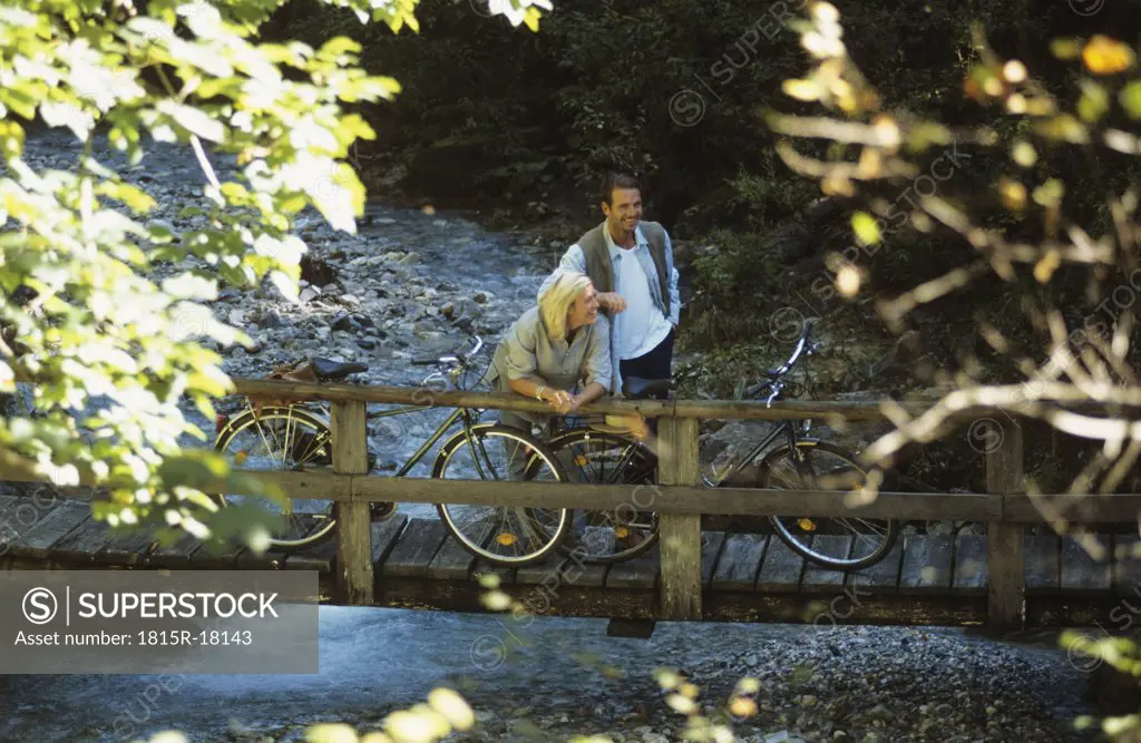 Couple with bicycles, standing on wooden bridge, smiling