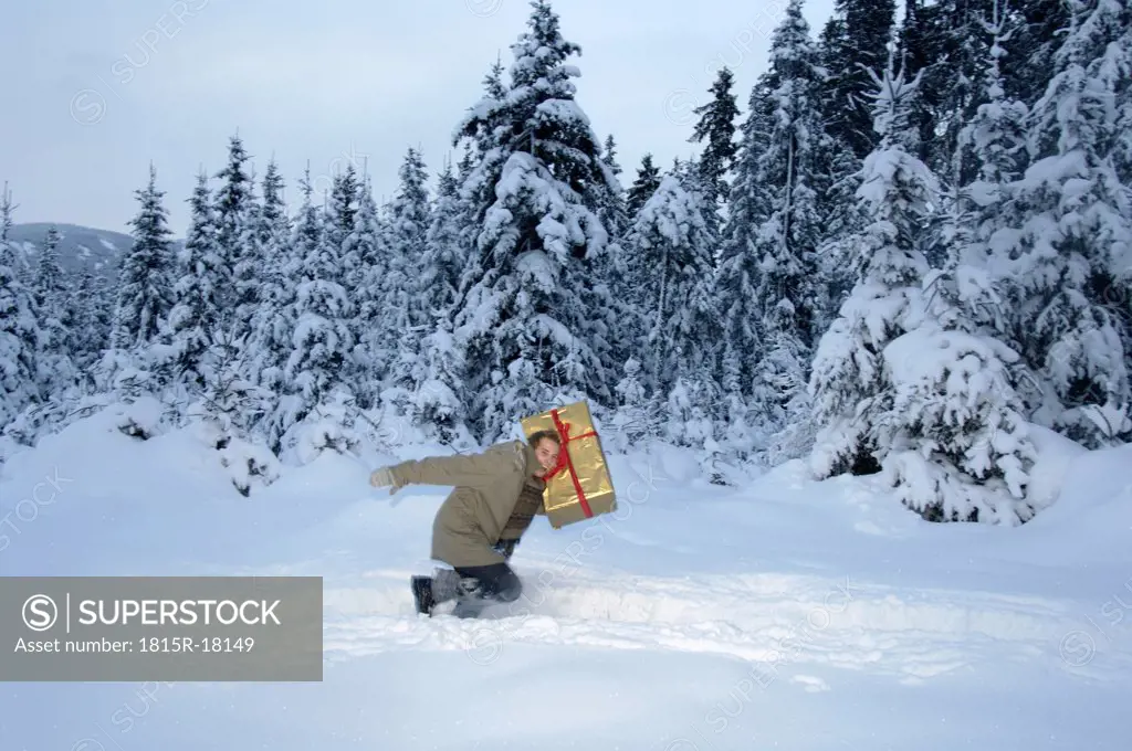 Young man carrying Christmas gift in snow, side view