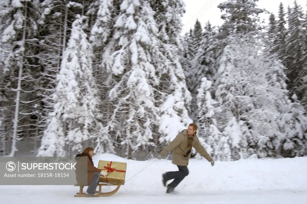 Young man pulling woman on sledge with Christmas gift