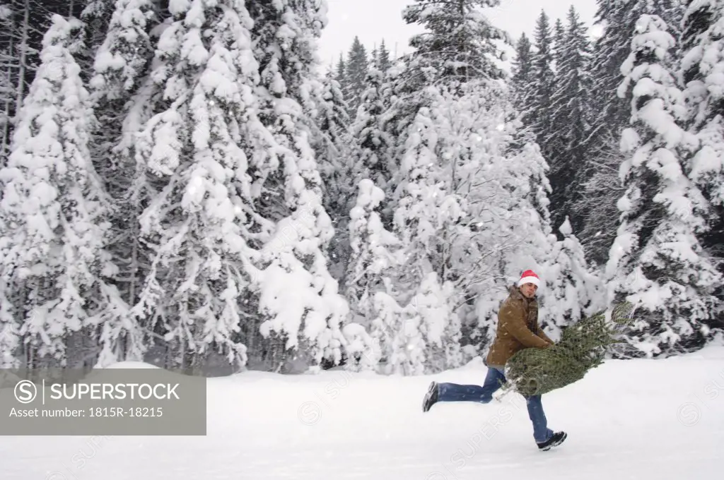 Man running in snow, carrying christmas tree