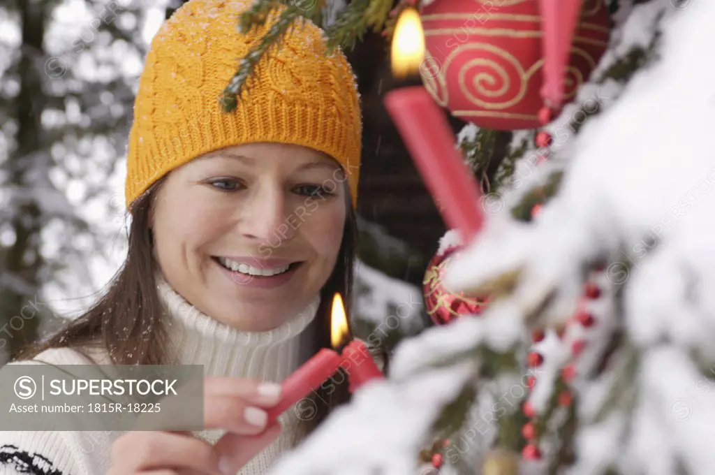 Young woman lighting candle on Christmas tree, smiling