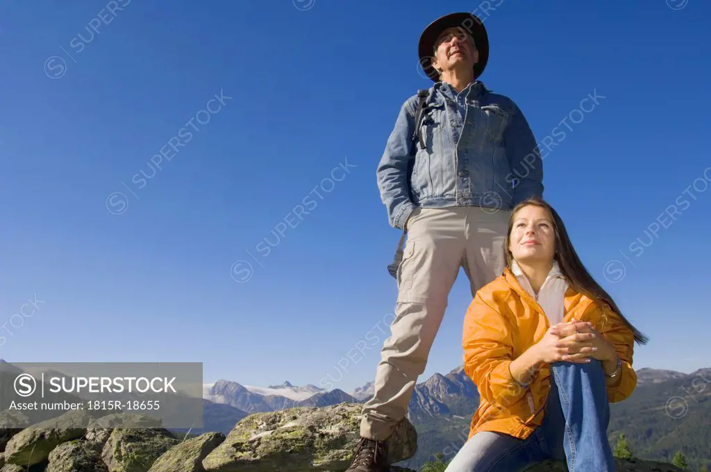 Couple in mountains, man standing, woman sitting on rocks
