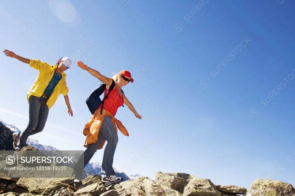 Two women walking on rock in mountains, arms out, low angle view