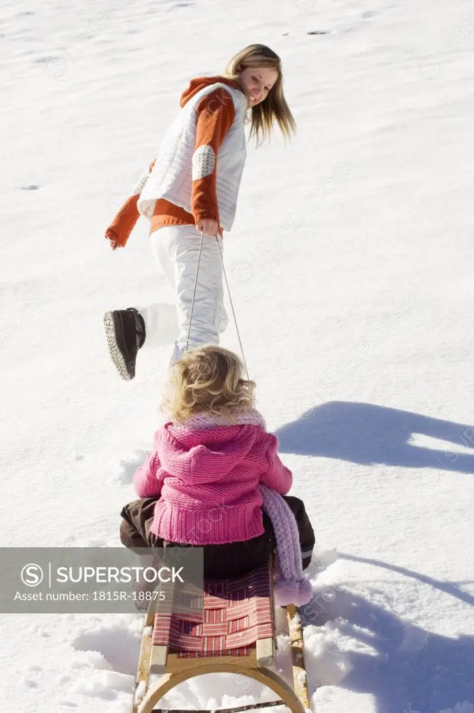 Girl sitting on sledge, mother pulling