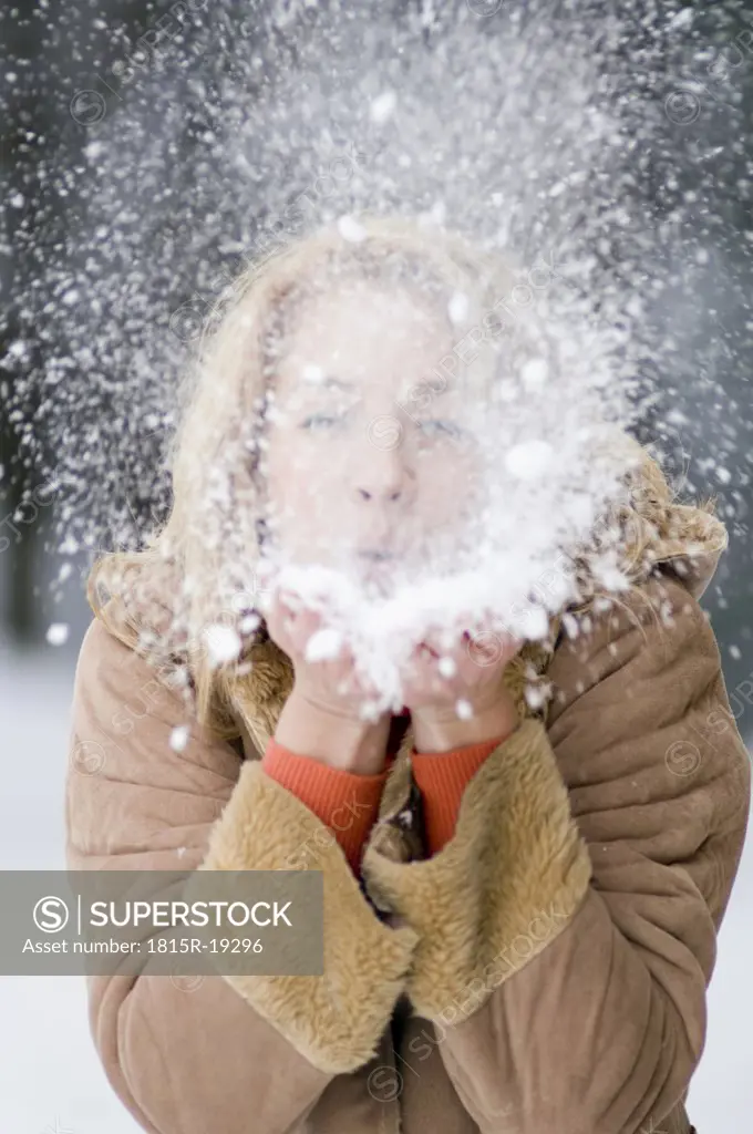 Austria, Salzburger Land, Altenmarkt, Young woman blowing snow off hand, portrait