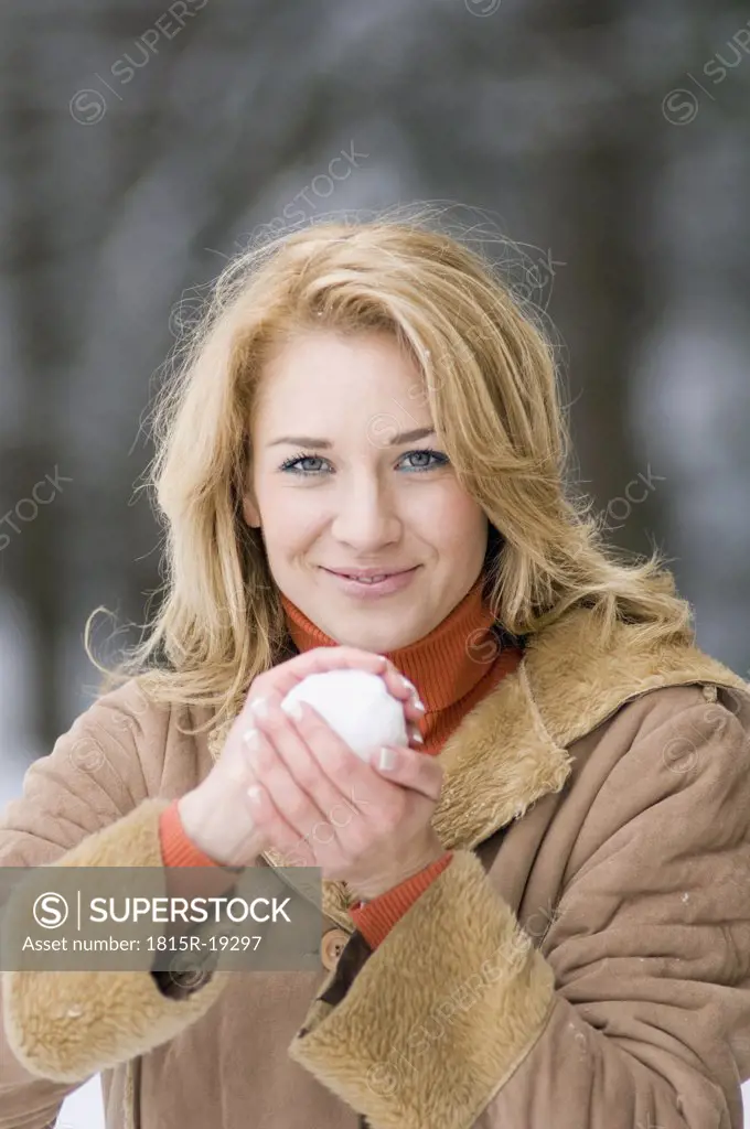 Austria, Salzburger Land, Altenmarkt, Young woman holding a snowball, smiling, portrait