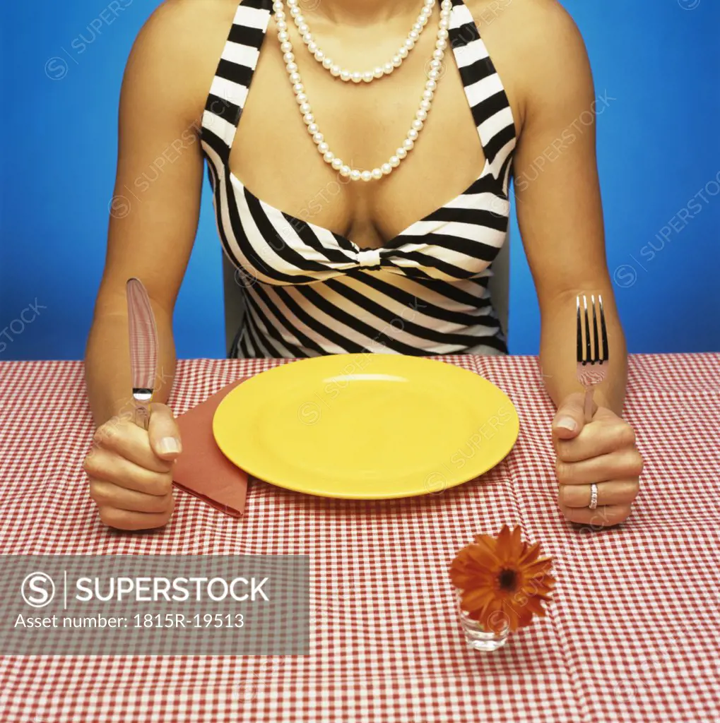Woman sitting at table with empty plate, holding cutlery