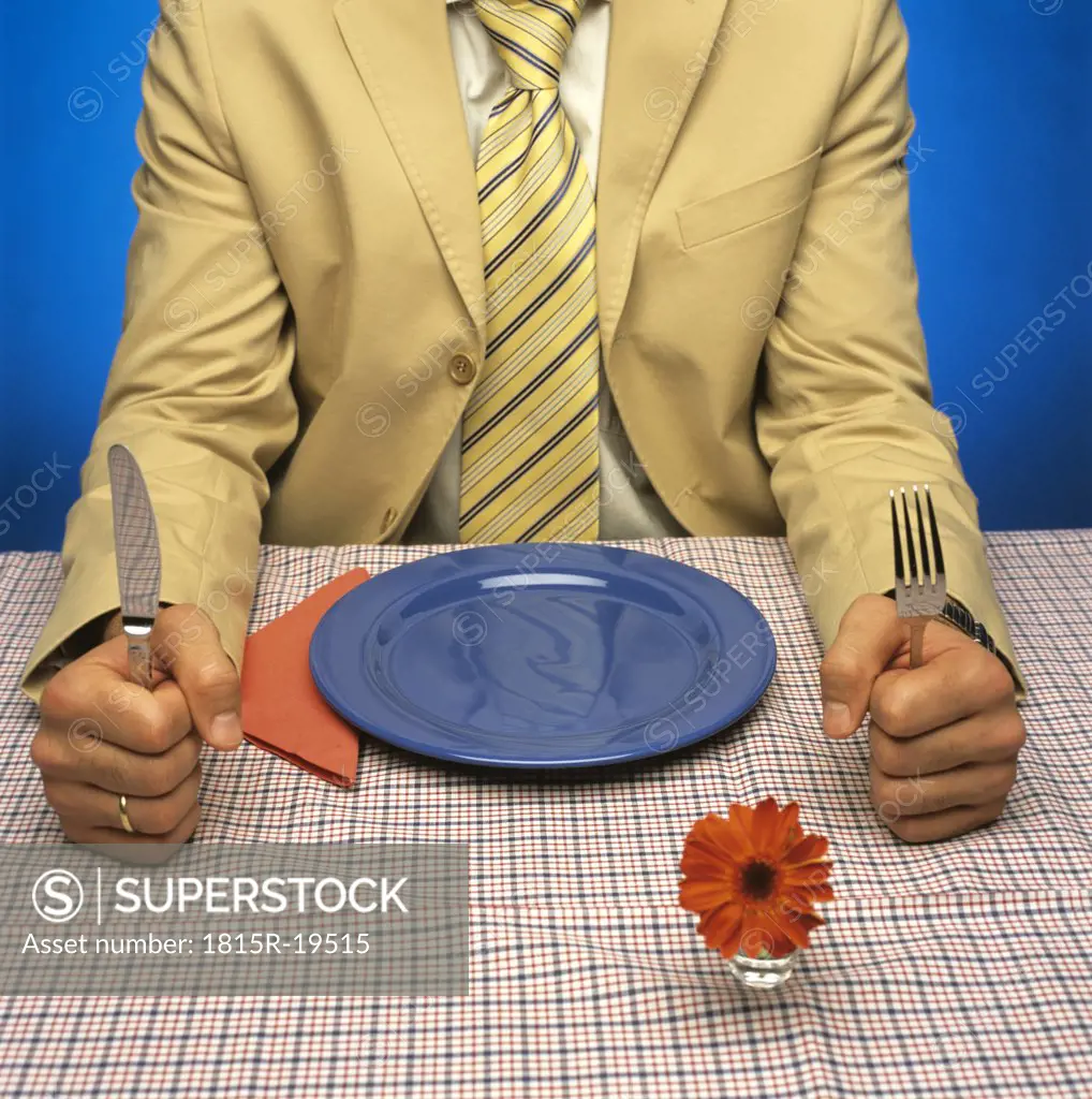 Man sitting at table with empty plate, holding cutlery