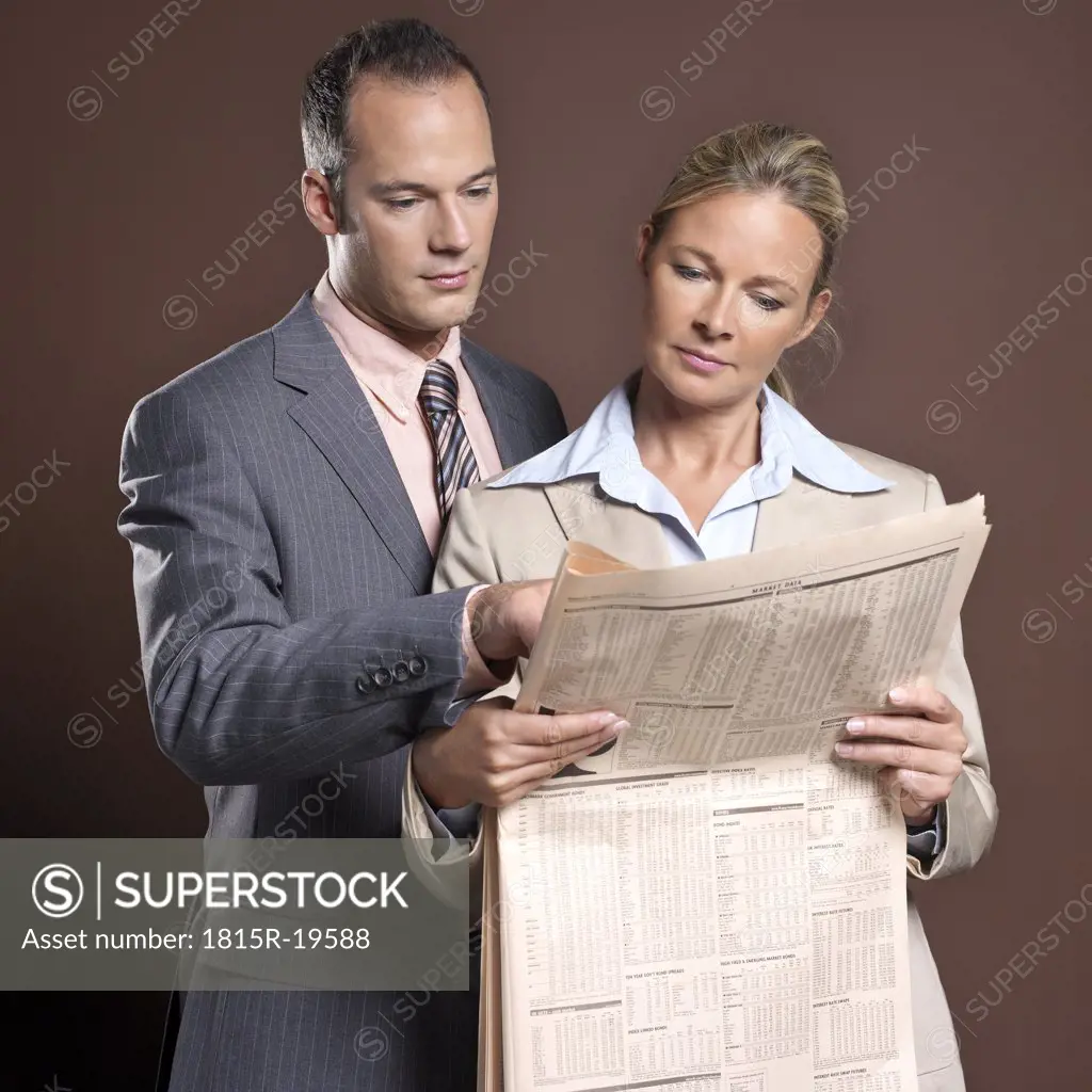 Businessman and businesswoman, holding newspaper