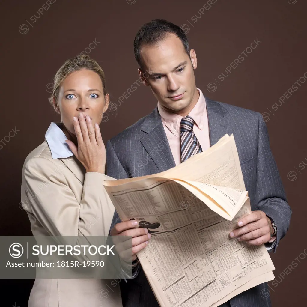 Businessman and businesswoman with newspaper, woman covering mouth