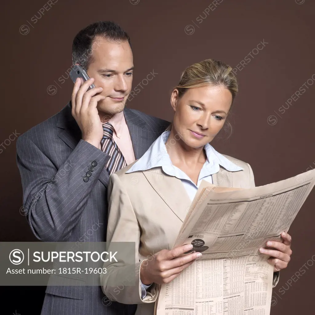 Businessman and businesswoman, man using mobile phone, woman holding newspaper