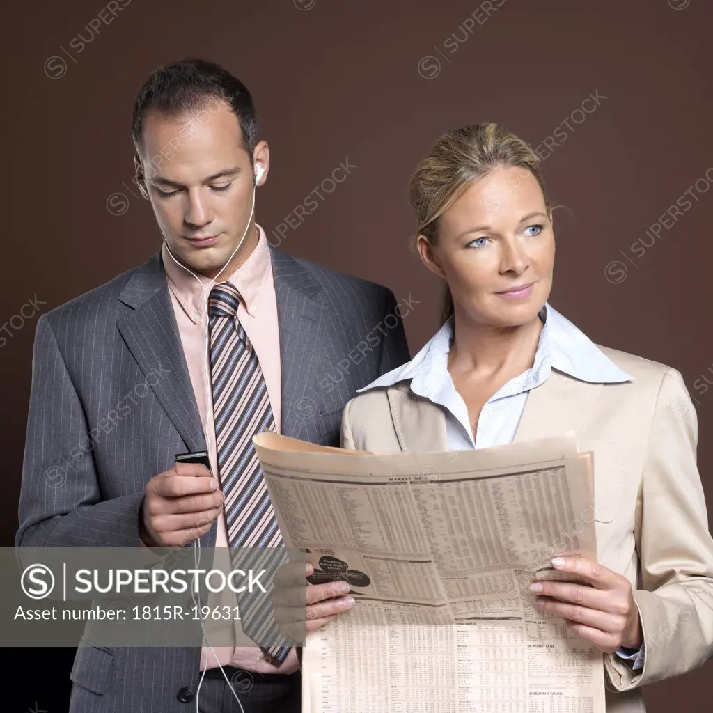 Businessman and businesswoman, man listening to mp3 player, woman holding newspaper