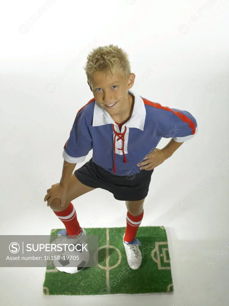 Boy (8-11) with foot on football, hand on hips