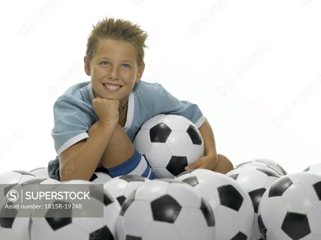 Boy (10-13) sitting between footballs