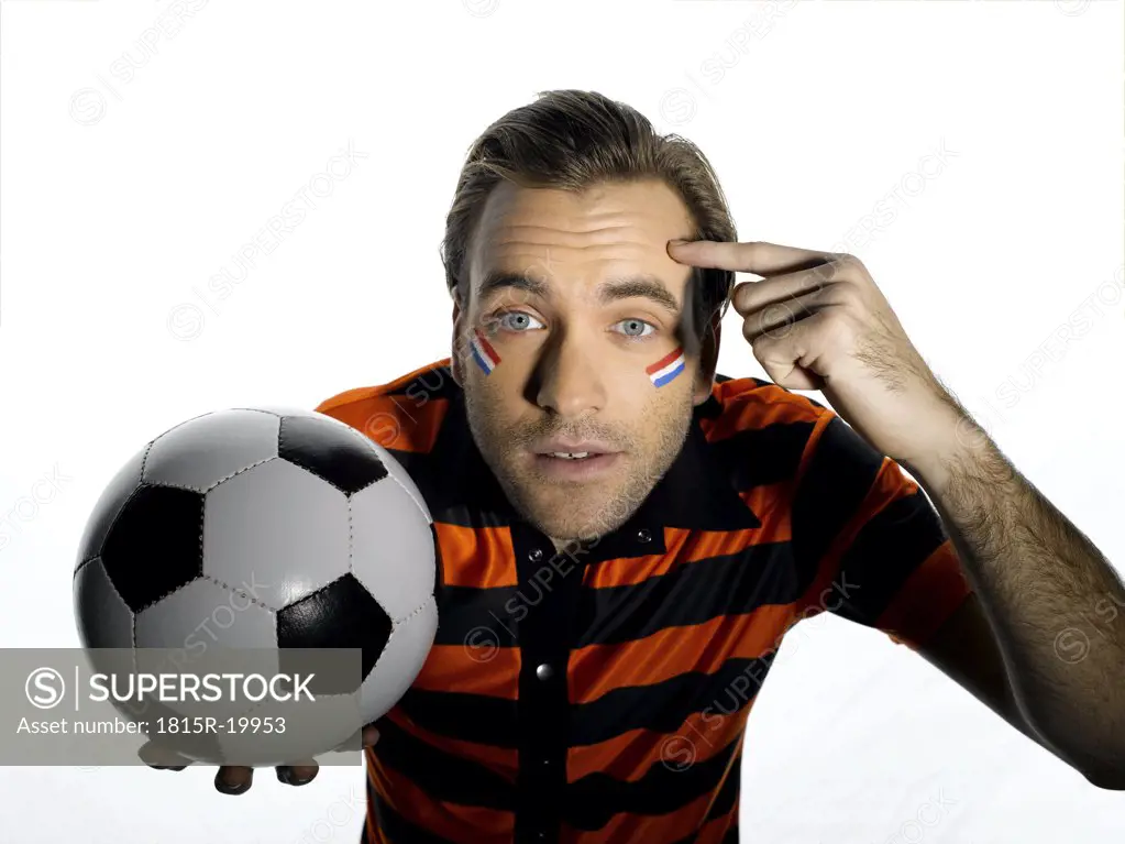 Man with Holland flag painted on face holding soccer ball, finger pointing on head, portrait