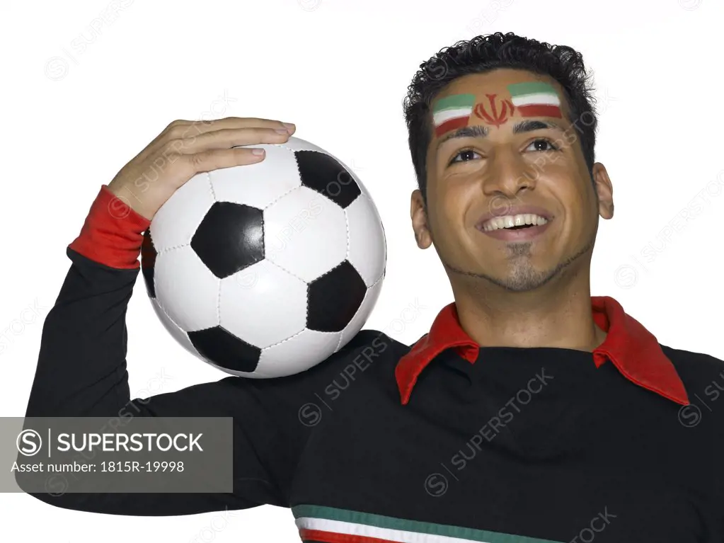 Young man with Iranian flag painted on face holding soccer ball, looking up