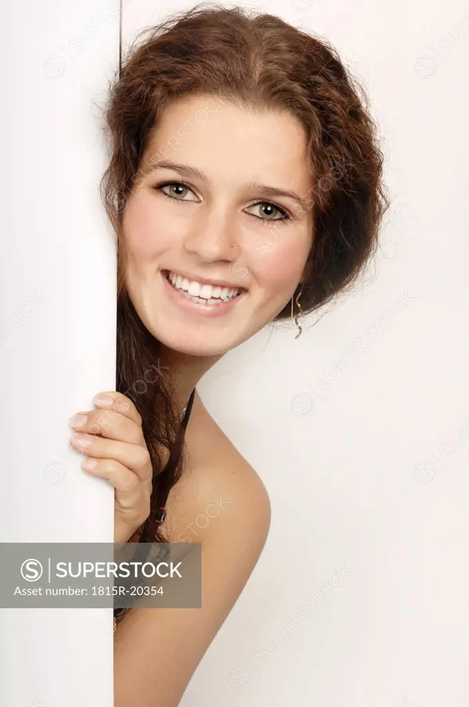 Young woman peeking through door, portrait, smiling