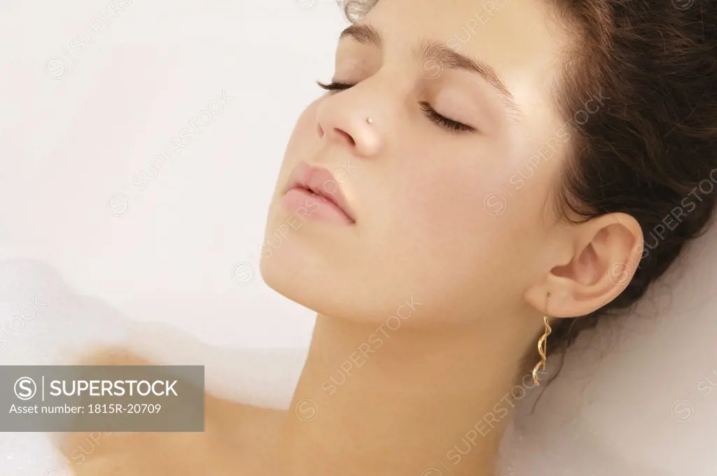 Young woman relaxing in bubble bath, eyes closed, close-up
