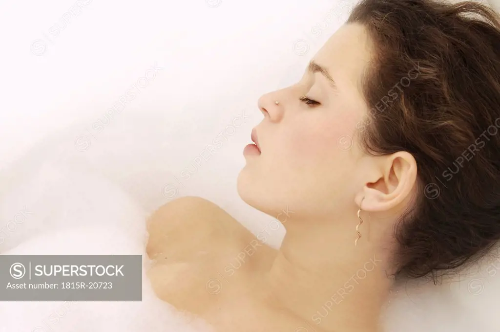 Young woman relaxing in bubble bath, eyes closed, close-up