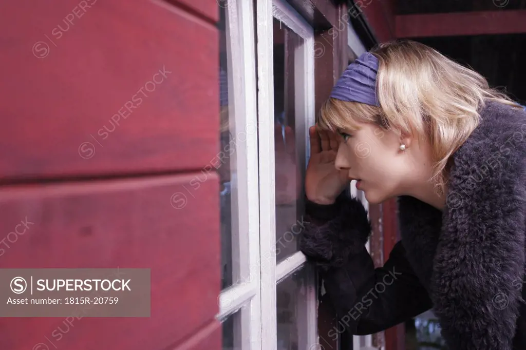 Young woman looking in house through window, side view