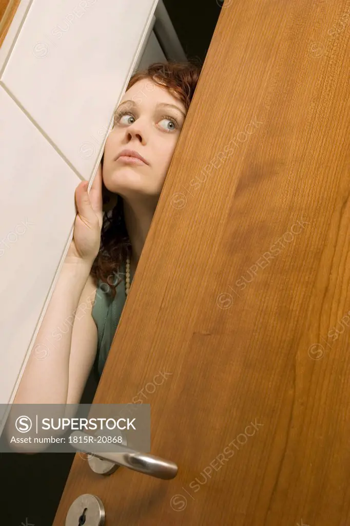Young woman peeking through door, close-up