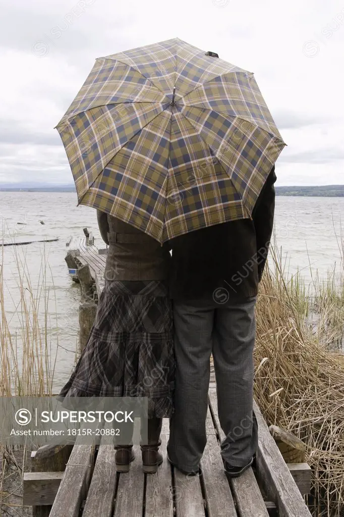 Couple on jetty with umbrella, rear view
