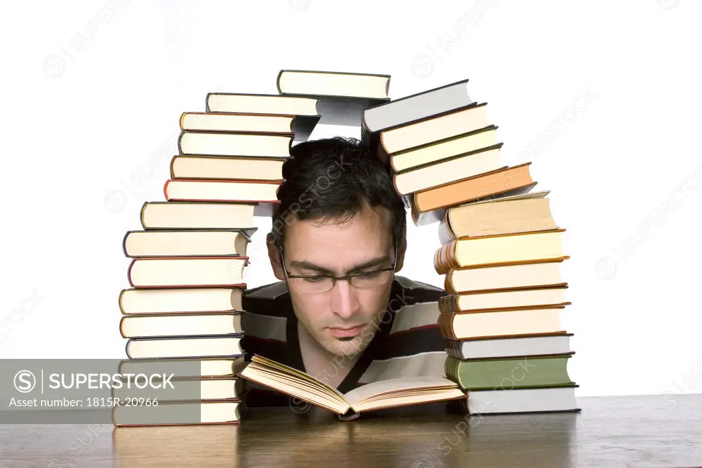 Young man reading by piled books, close-up