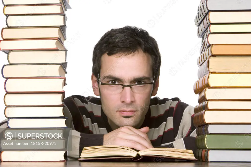 Young man reading by piled books, portrait, close-up