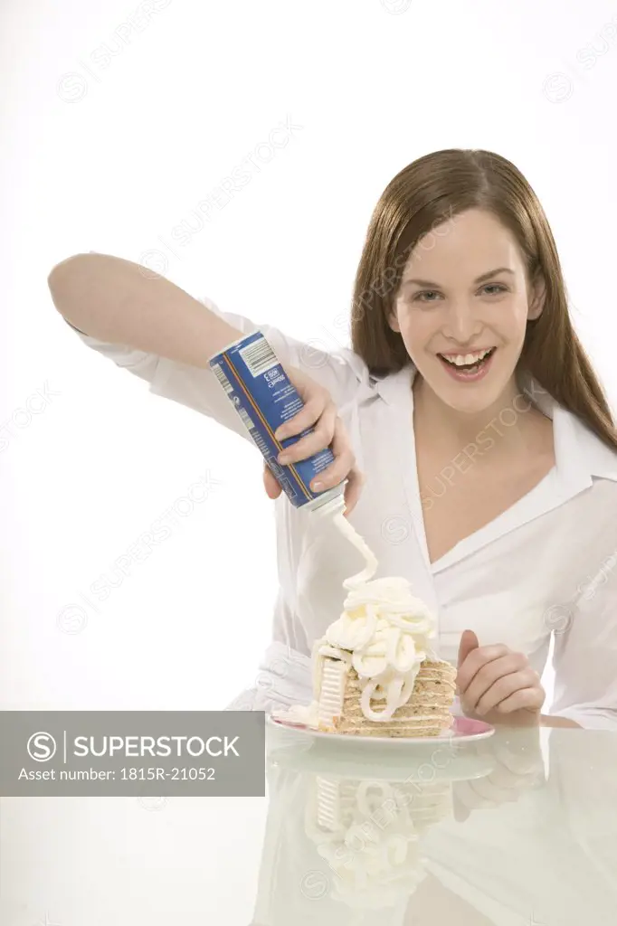 Young woman spraying cream on cake, portrait