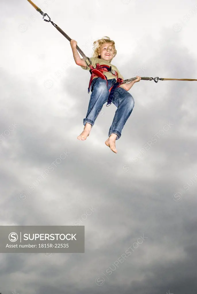 Boy (10-11) on bungee swing, smiling, low angle view