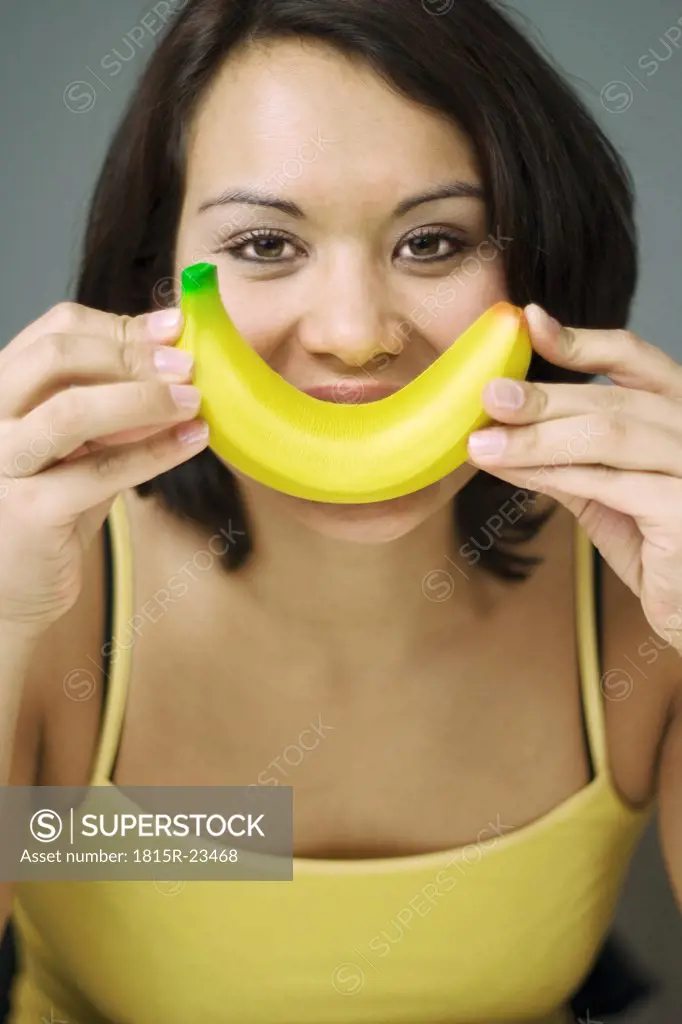 Young woman holding banana to mouth, close-up, portrait