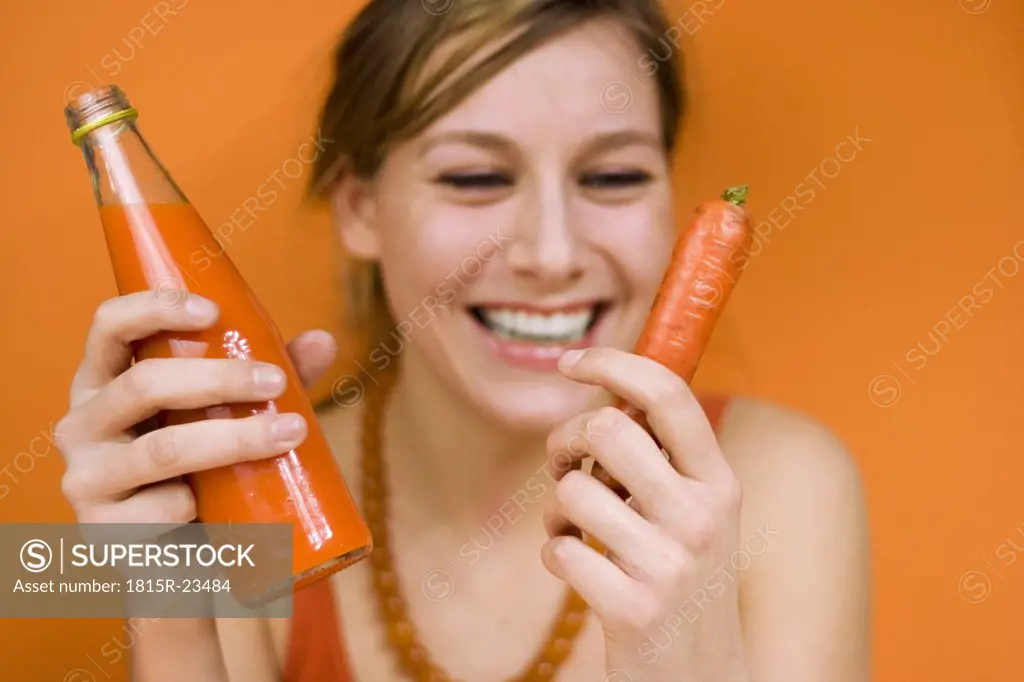 Young woman holding carrot and carrot juice, smiling, close-up