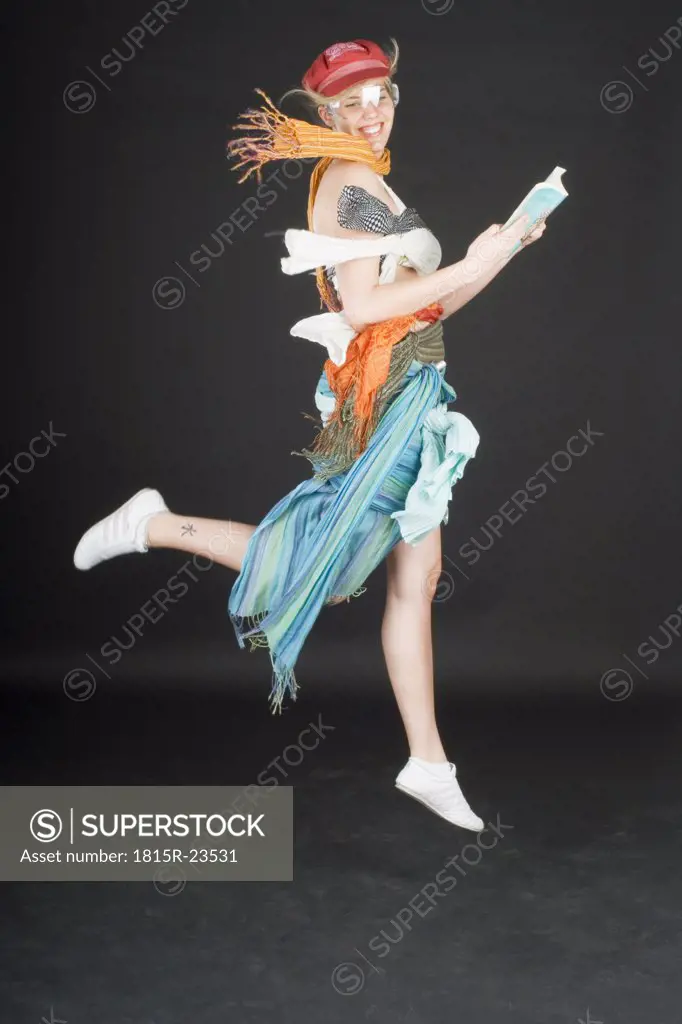 Young woman jumping, holding book, smiling, side view