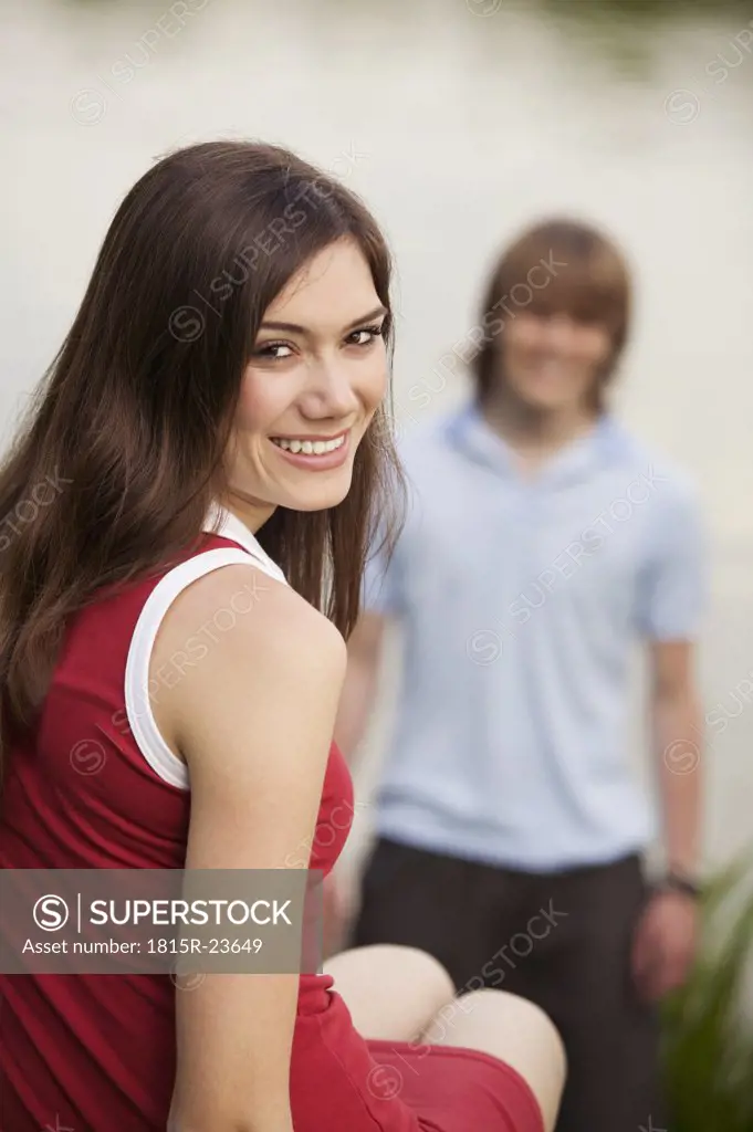 Young woman smiling, young man in background
