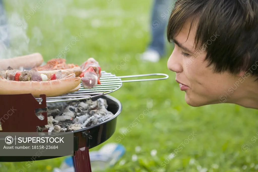 Young man by grill with meat, side view, close-up
