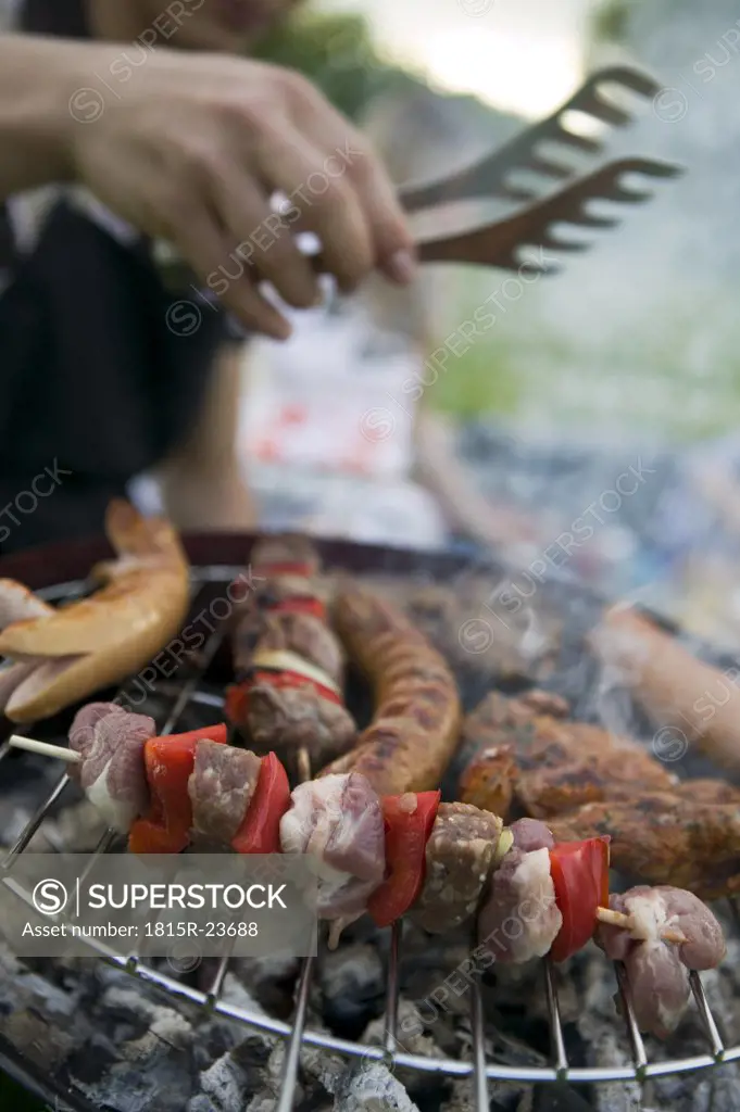 Meat and sausages on grill, people in background