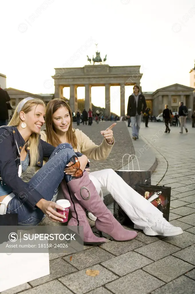 Two young woman with shopping bags sitting on pavement