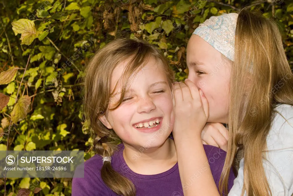 Girl (8-11) whispering in friend's ear, smiling