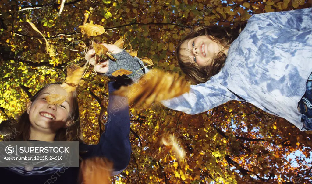 Girls (8-13) with autumn leaves, low angle view, portrait