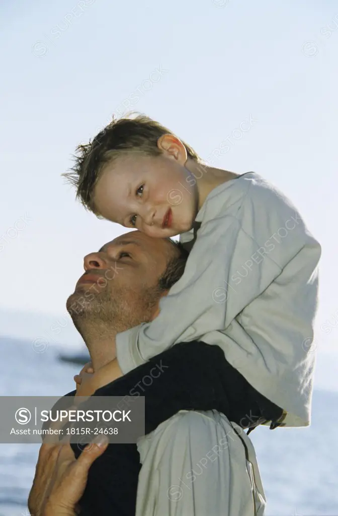 Father carrying boy (4-7) on shoulders by sea