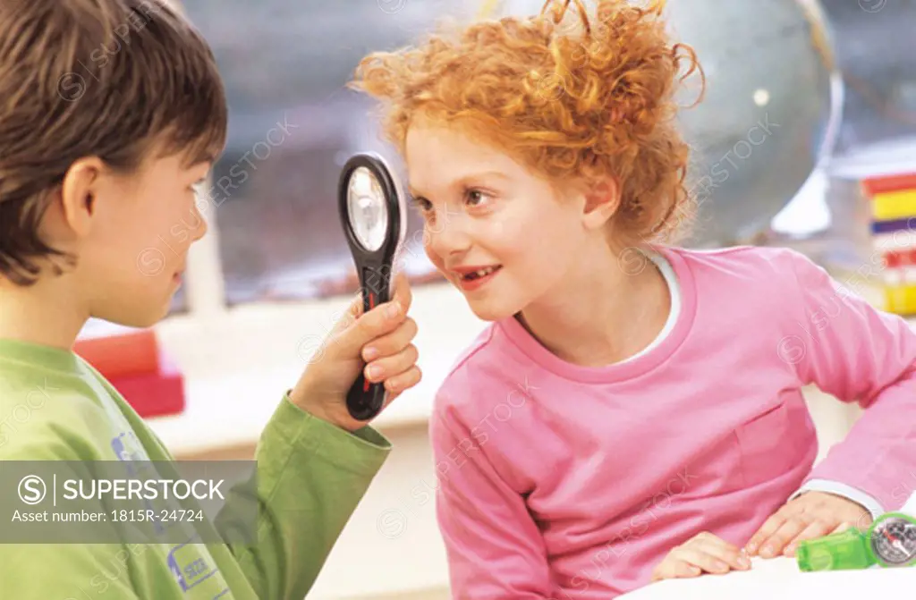 Boy and girl (6-9) looking at eachother with magnifying glass