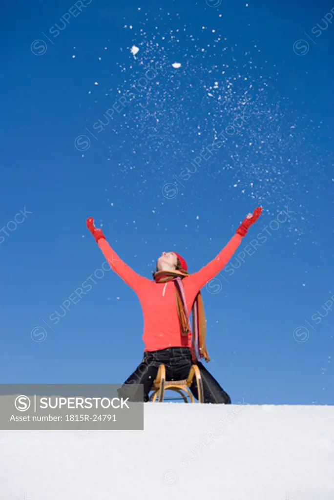 Woman sitting on sledge with arms outstretched, low angle view