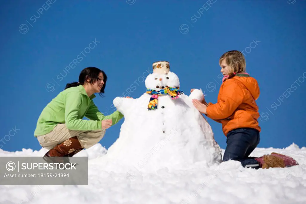 Austria, girls (12-17) making snowman, side view