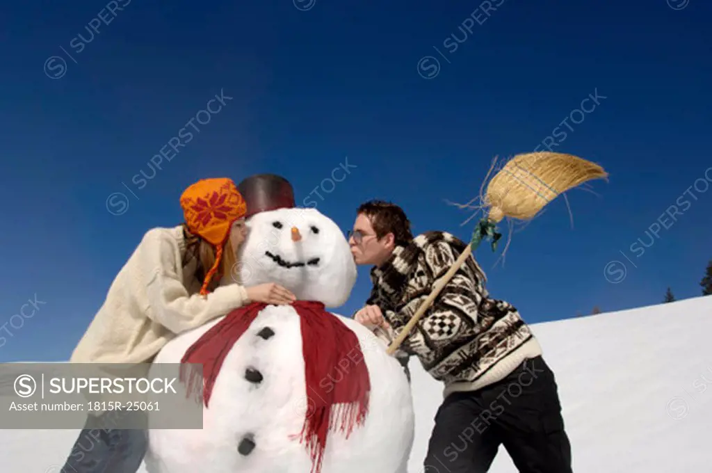 Young couple kissing snow man, low angle view