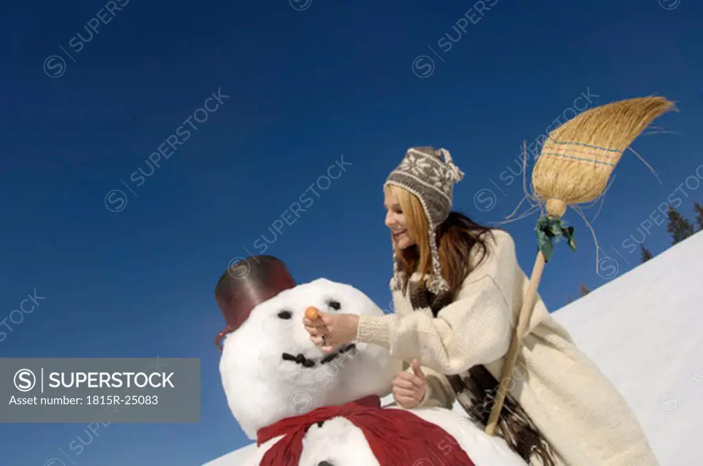 Young woman making snowman, smiling, low angle view